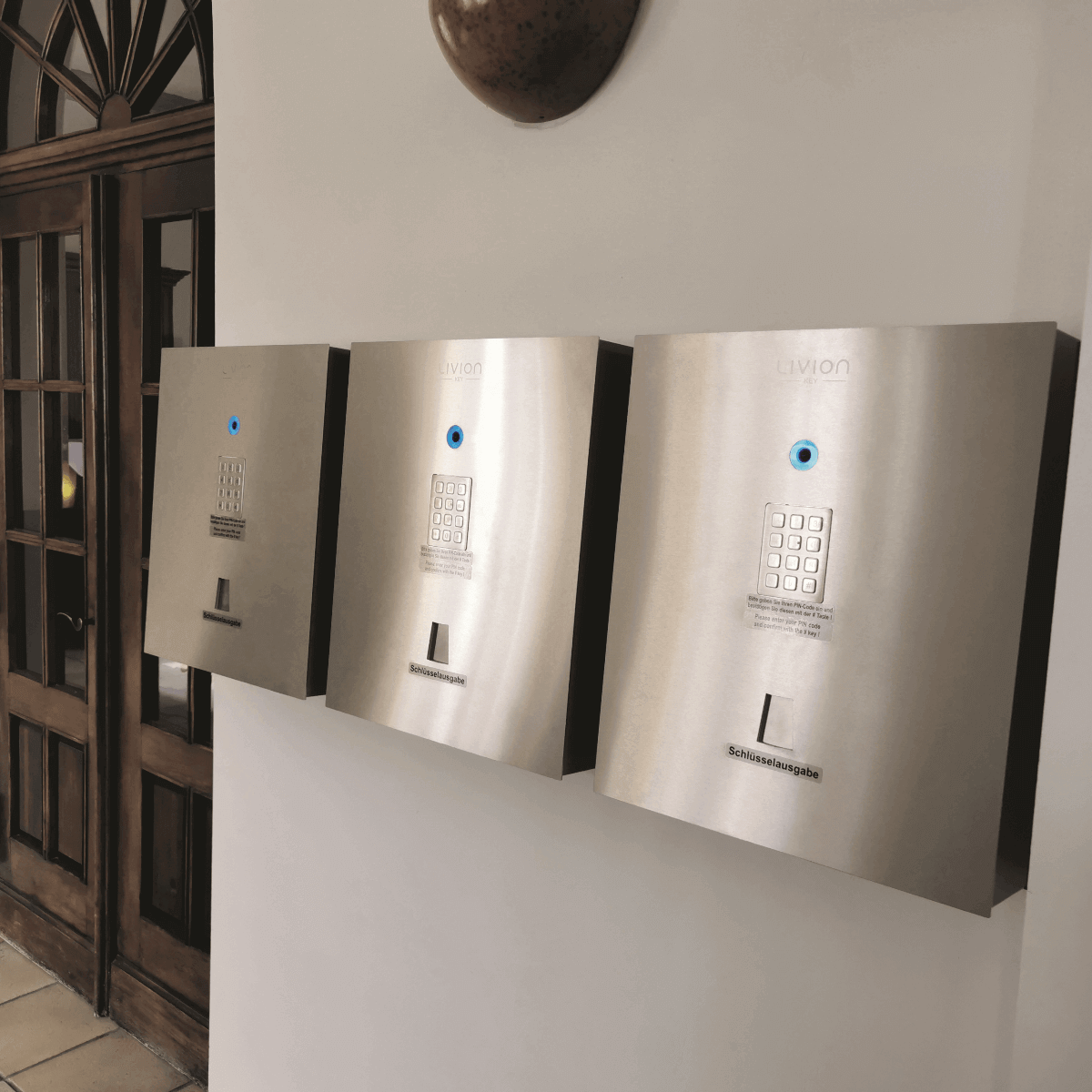 Elektronisches Schlüsselausgabesystem Livion aus Edelstahl mit Tastenfeld für sicheren Zugang Drei moderne, an der Wand montierte Schlüsselausgabesysteme aus Edelstahl mit Tastenfeld und blauem LED-Licht