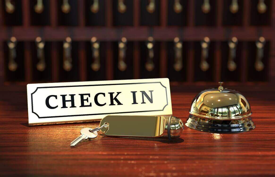 Hotelrezeption mit Check-in-Schild, Metallschlüssel und goldenem Empfangsglöckchen auf einem Holztresen