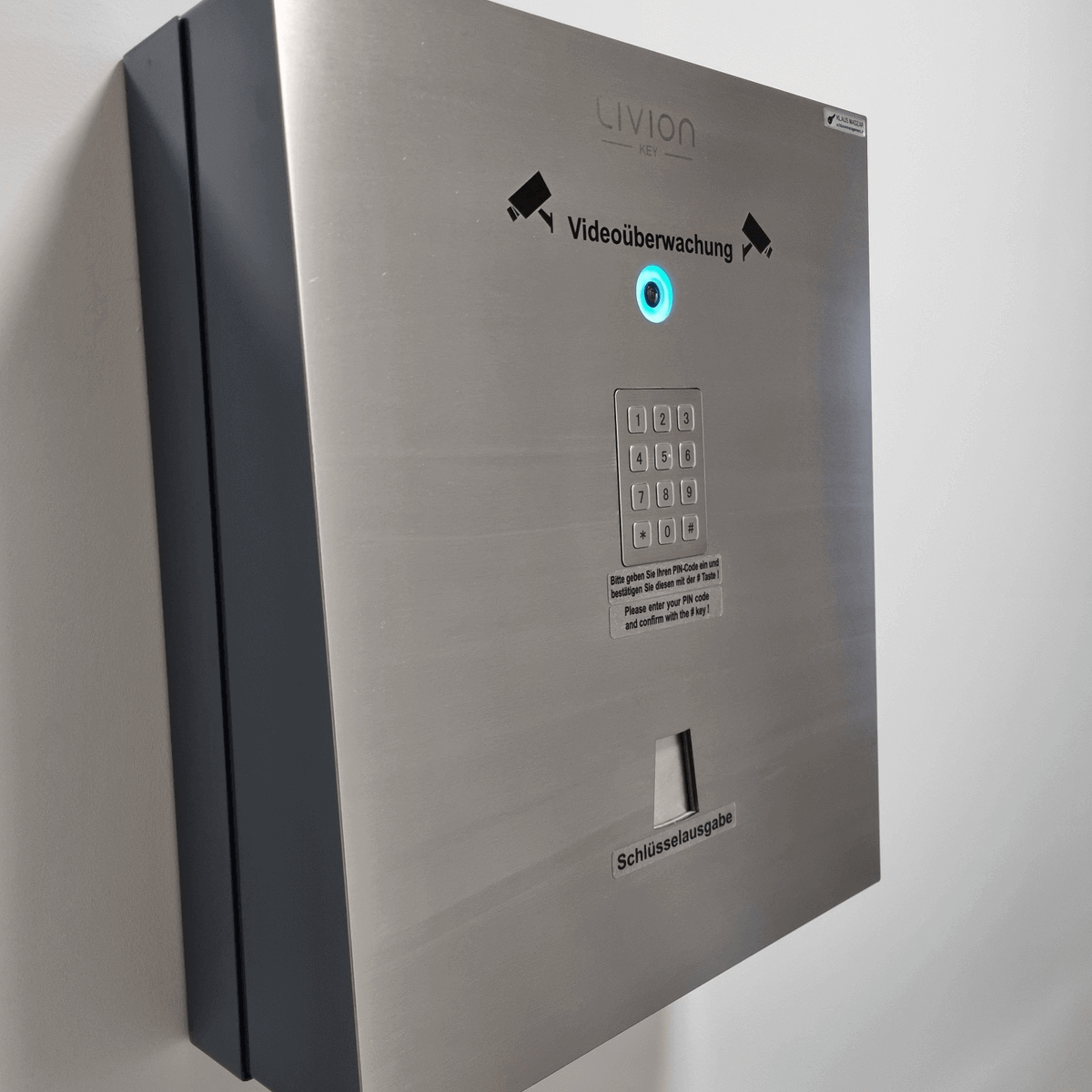 Schlüsselausgabe-Automat mit PIN-Tastatur und Videoüberwachung Metallischer Schlüsselausgabe-Automat mit PIN-Pad und Videoüberwachungshinweis an einer Wand montiert