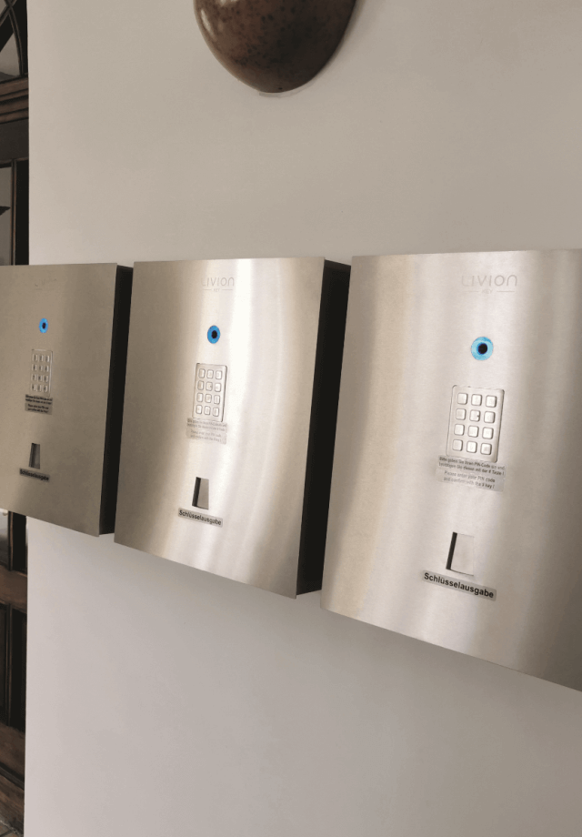Drei Schlüsselausgabesysteme aus Edelstahl mit Zahlentastatur und blauem Lichtring, montiert an einer Wand