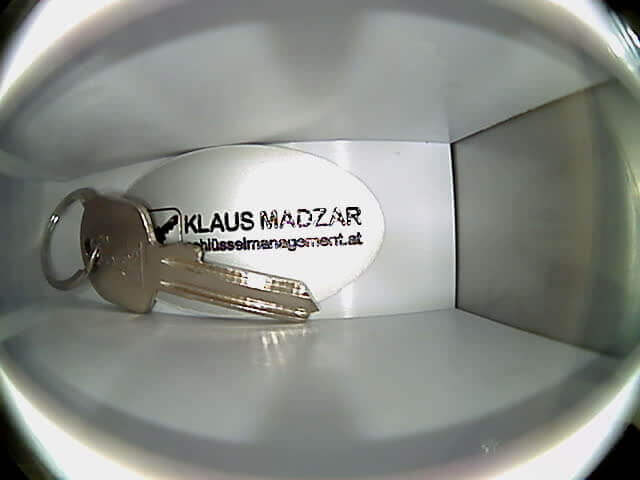 Zwei Hausschlüssel mit Anhänger im Schließfach von Klaus Madzar Schlüsselmanagement Zwei silberne Schlüssel an einem Schlüsselring mit Anhänger, auf dem 'Klaus Madzar schluesselmanagement.at' steht, in einem weißen Schließfach