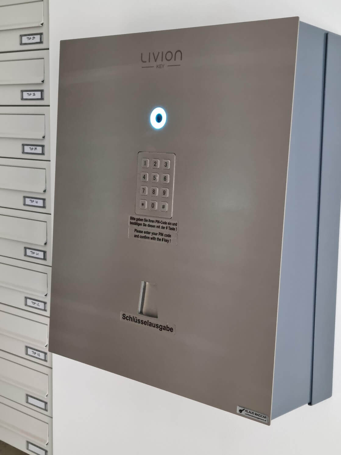 Elektronischer Schlüsselausgabe-Automat LIVION KEY mit PIN-Eingabe für sichere Schlüsselübergabe Schlüsselausgabe-Automat LIVION KEY mit beleuchtetem Tastenfeld und PIN-Codierung neben Briefkastenanlage