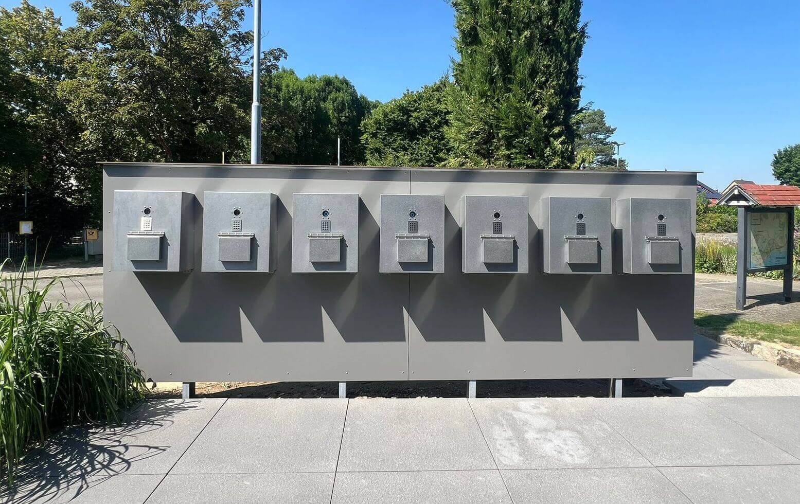 Mehrere moderne Livionkey30 Schlüsseldepots im Außenbereich mit Zahlenschloss Sieben graue Schlüsseldepots Livion mit Zahlenschlössern im Außenbereich vor Bäumen bei sonnigem Wetter