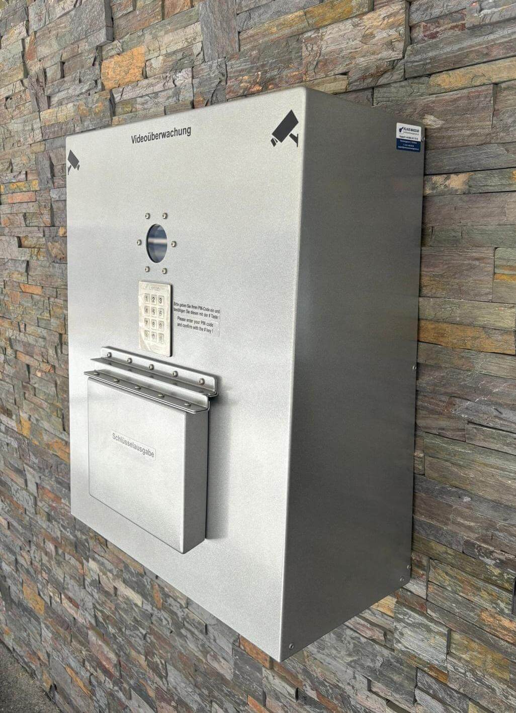 Schlüsselausgabe mit Videoüberwachung und Zahlencode an einer Steinwand Metallene Schlüsselausgabe-Station mit Videoüberwachung und Zahlencode-Tastatur, montiert an einer Steinwand