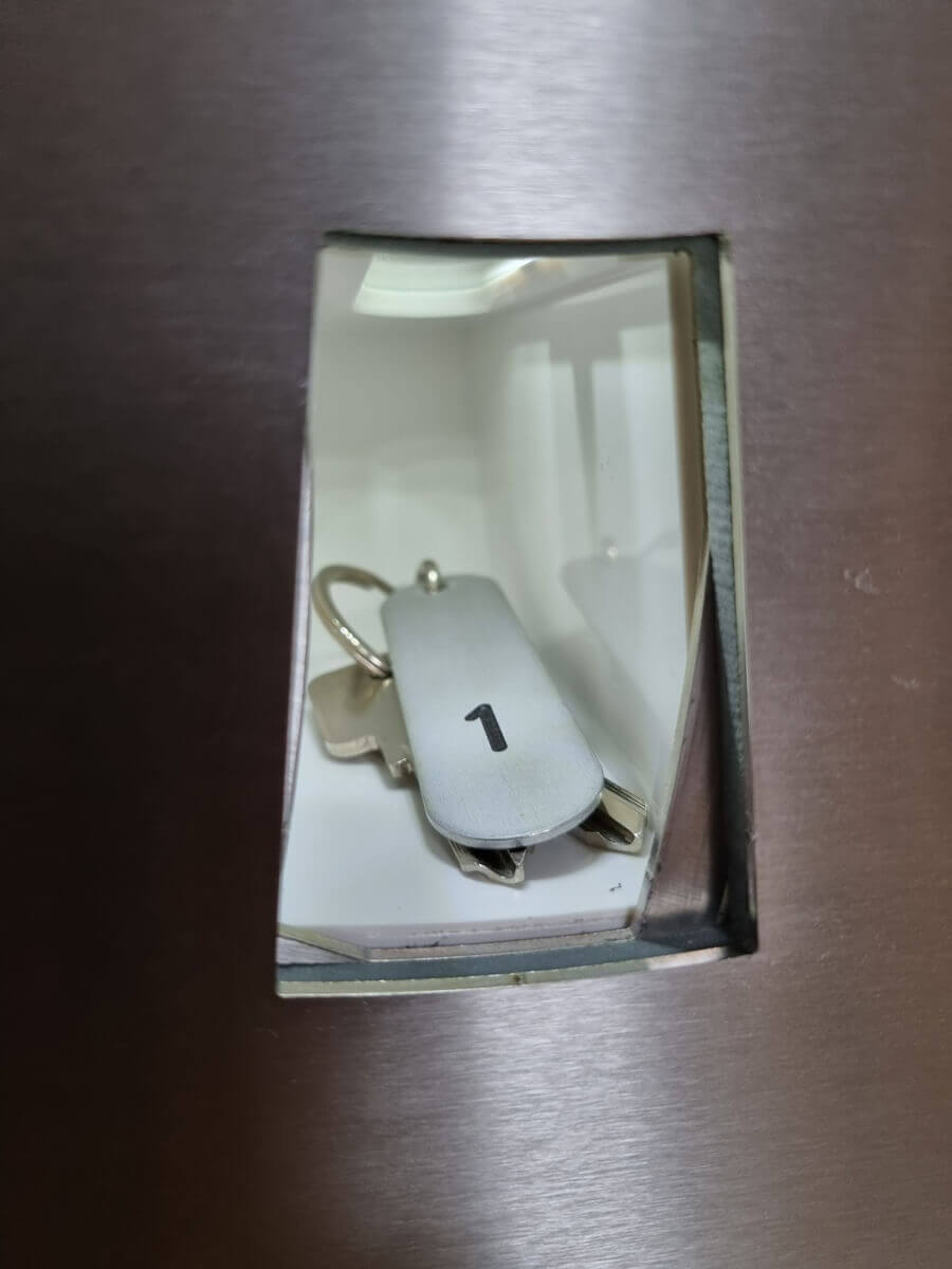 Schlüssel mit Anhänger Nummer 1 in Metallschacht Ein Metallschlüssel mit einem Schlüsselanhänger, der die Zahl 1 trägt, liegt in einem kleinen Metallschacht.