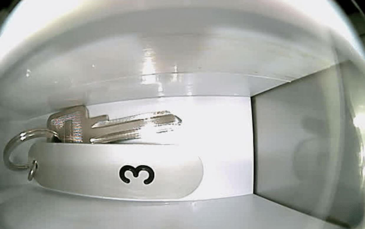 Schlüssel mit Schlüsselanhänger und Zahl 3 in einem weißen Fach Ein silberner Schlüssel mit einem Schlüsselanhänger, auf dem die Zahl 3 steht, liegt in einem weißen Ablagefach.