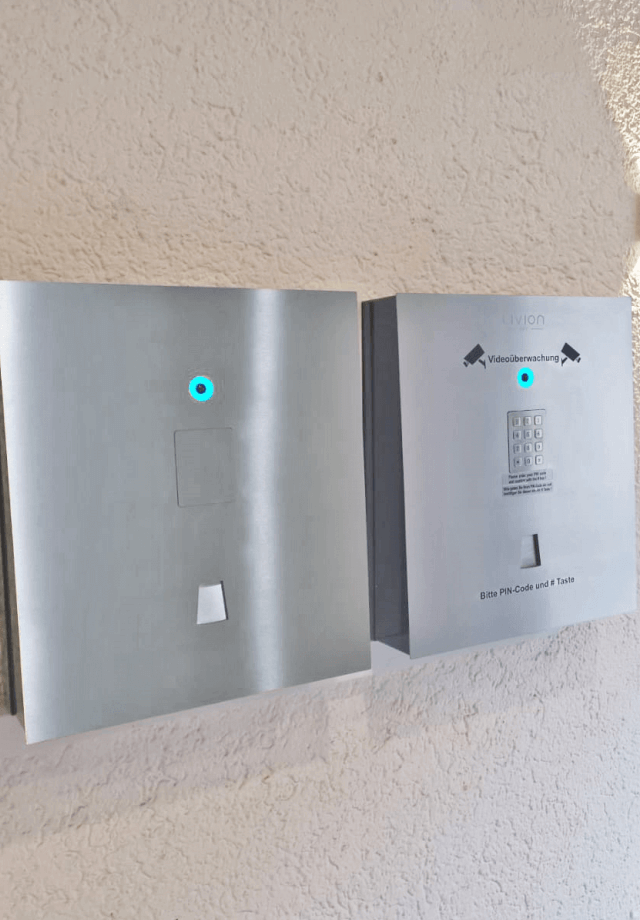 Zugangskontrollsystem mit PIN-Eingabe und Videokamera, montiert an einer Wand, in einem Edelstahlgehäuse.