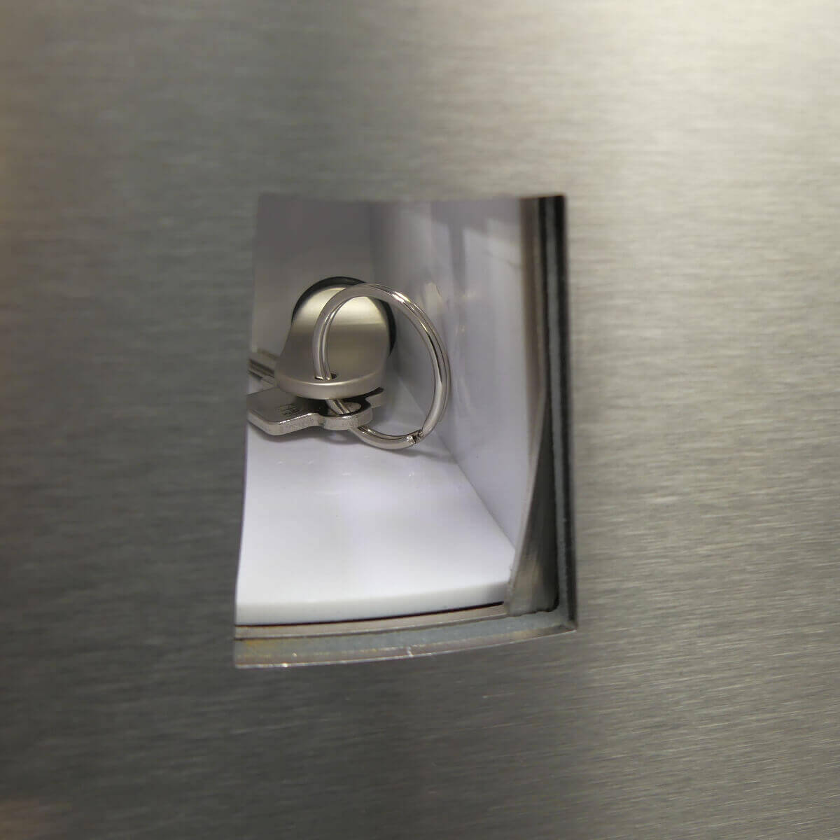 Ein Schlüsselbund mit silbernem Schlüsselanhänger liegt in einem Fach eines Metallschranks.