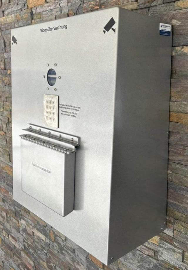 Metallischer Sicherheitsschrank an einer Steinwand mit integrierter Videokamera, Tastatur und Schlüsselausgabe