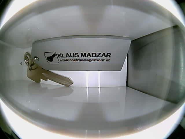 Schlüssel mit Anhänger von Klaus Madzar im Schließfach Ein Schlüssel mit Anhänger liegt in einem weißen Schließfach, der Anhänger trägt die Aufschrift 'Klaus Madzar schlüsselmanagement.at'.