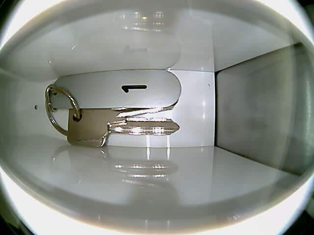 Metallschlüssel mit rechteckigem Schlüsselanhänger auf weißer Oberfläche Ein einzelner Metallschlüssel mit einem rechteckigen Schlüsselanhänger liegt auf einer glatten, weißen Fläche in einer Box oder einem Fach