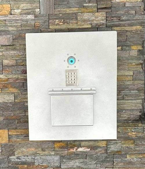Moderner Edelstahl-Schlüsselautomat mit Zahlenschloss und Klingel an Steinwand Edelstahl-Briefkasten mit integriertem Zahlenschloss, Klingel und Kamera vor einer Steinwand