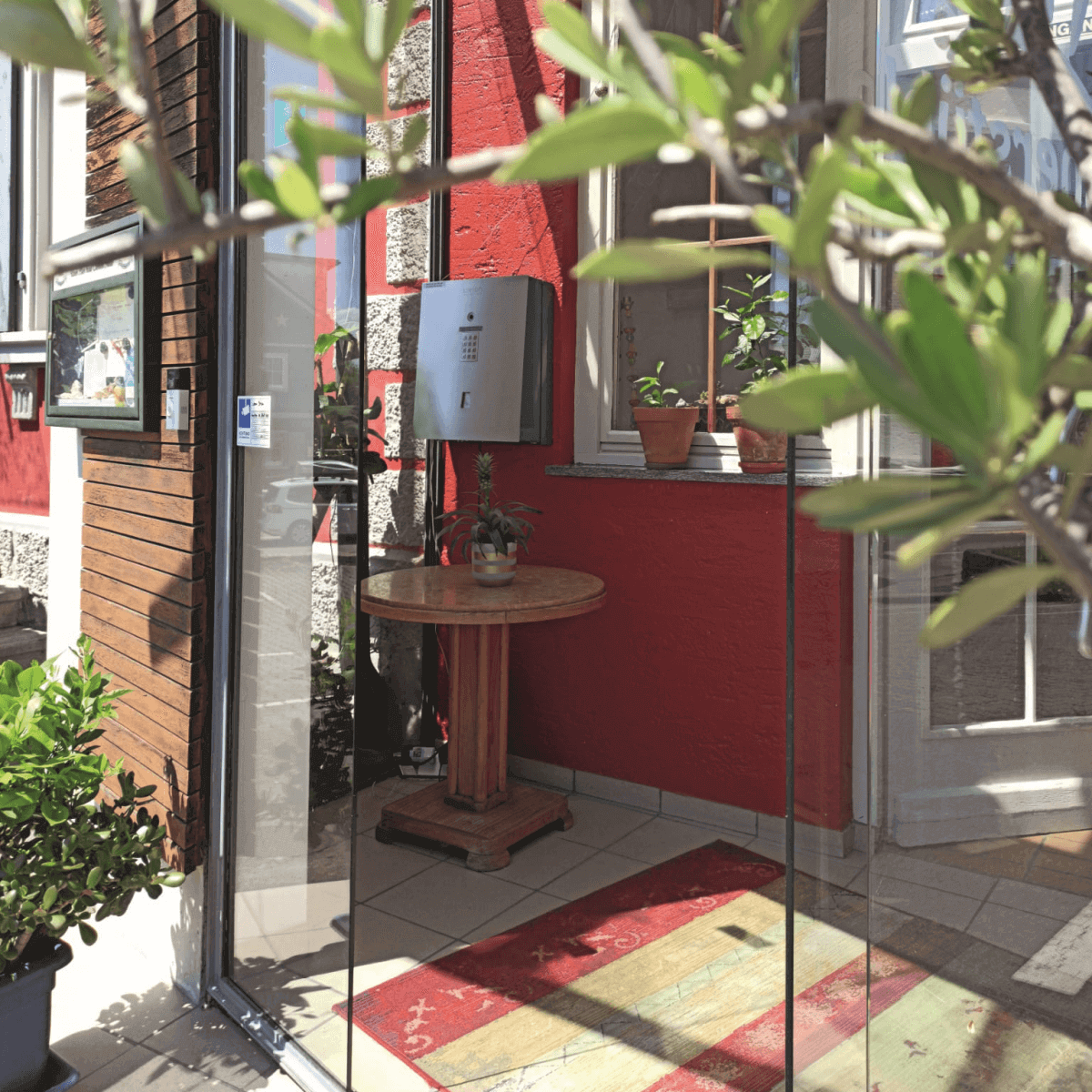 Eingangsbereich mit roter Wand, Holztisch und Pflanzen bei Tageslicht Heller Eingangsbereich mit Glastür, kleinem Holztisch, Zimmerpflanzen und roter Wand im Hintergrund