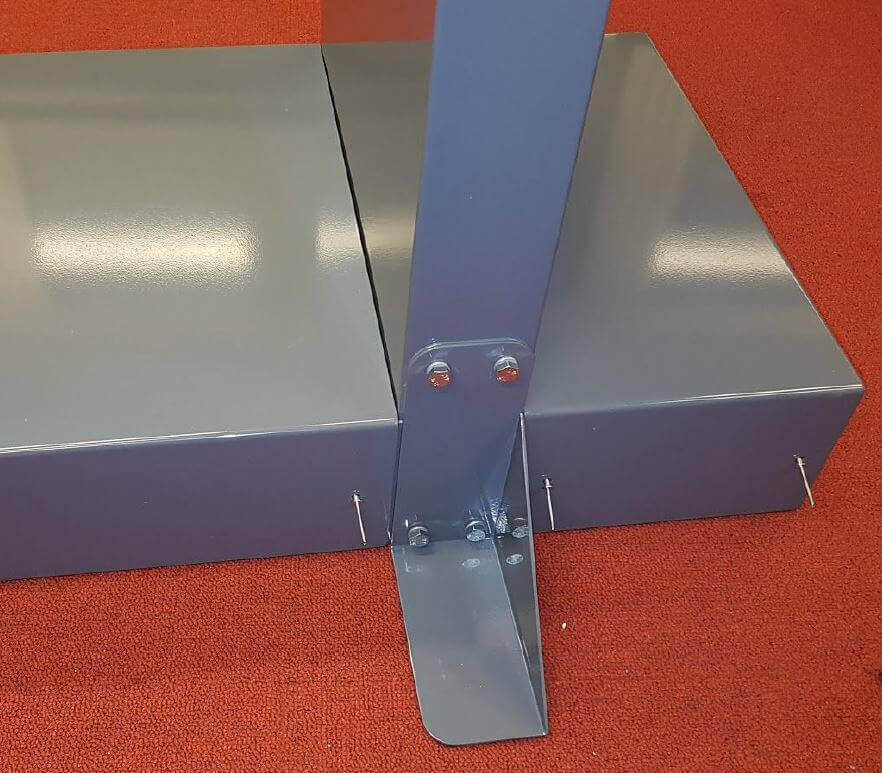 Stabile Metallkonstruktion mit verschraubter Bodenplatte auf rotem Teppichboden Detailaufnahme einer verschraubten Stahlkonstruktion mit Bodenplatte und rotem Teppichuntergrund