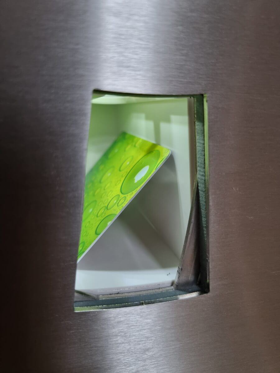 Grüne Chipkarte in der Ausgabeöffnung eines Automaten Nahaufnahme einer grünen Chipkarte mit Kreismuster, teilweise sichtbar in der Ausgabeklappe eines silbernen Automaten