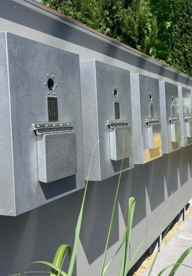 Mehrere graue Metallbriefkästen mit Zahlenschlössern an einer Wand im Freien